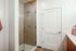Modern bathroom with a glass-enclosed walk-in shower, neutral-toned horizontal tile, and a sleek wood vanity partially visible on the right.