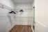 Empty walk-in closet with white wire shelving, wooden floor, a full-length mirror leaning against the wall, and dark wooden hangers on racks.