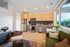 Modern open-concept kitchen with light wood cabinetry, stainless steel appliances, a green couch, large window, and cozy living area accents.