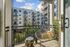 Private apartment balcony with a modern outdoor chair and accent pillows, overlooking a courtyard and surrounding apartment buildings under a blue sky.