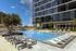 Modern apartment building with a stunning outdoor swimming pool and lounging area under a clear blue sky.
