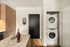 Stylish apartment entrance featuring modern kitchen cabinetry, a black door, and a stacked washer-dryer unit.