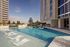 Stunning rooftop pool area with modern lounging chairs, surrounded by lush greenery and high-rise views.