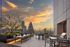 Breathtaking sunset view from a modern rooftop terrace overlooking a city skyline with lush greenery and seating.
