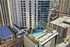 Aerial view of a modern high-rise building with a rooftop swimming pool and lush garden area in a bustling cityscape.