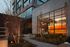 Modern apartment building exterior with large glowing windows and vibrant garden, creating a warm evening ambiance.