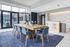 Modern communal space with elegant wooden table, stylish blue chairs, and chic bar area, bathed in natural light from large windows.