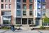 Modern apartment building exterior with large windows and landscaped entrance, featuring a cyclist passing by.