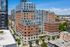 Modern urban apartment complex with a blend of brick and glass facades, featuring lush rooftop gardens and a vibrant cityscape backdrop.