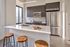 Modern kitchen with sleek appliances, dark cabinetry, and a stylish breakfast bar featuring natural wood stools in a sunlit apartment.