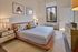 Elegant bedroom featuring a plush bed with decorative pillows, chic artwork, and a stunning city view through a large window.