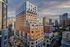 Modern urban apartment building with stylish brick and glass facade, featuring spacious balconies and vibrant city views under a dramatic sky.
