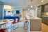 Contemporary open-plan kitchen and living area featuring sleek appliances, a stylish breakfast bar with stools, and a chic dining setup with red chairs and modern lighting.