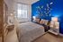 Modern bedroom with vibrant blue accent wall, stylish geometric decor, and cozy lighting, offering a serene city view through a large window.