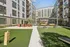 Modern apartment courtyard featuring lush green lawn, seating area, and vibrant orange bar stools under string lights, ideal for relaxation and entertainment.