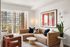 Modern living room with plush tan sectional sofa, vibrant artwork, and large windows offering a stunning city view.