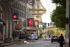 Vibrant city street view with elegant overhead chandelier and bustling activity, lined with charming buildings and colorful signage.