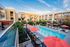 Luxurious apartment complex featuring a sparkling swimming pool and vibrant red umbrellas, set against modern architecture and lush greenery.