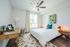 Bright and cozy bedroom with a sleek wooden office desk, modern ceiling fan, and large window providing ample natural light.