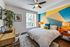 Modern bedroom with geometric accent wall, cozy bed, and natural light streaming through a large window overlooking lush greenery