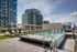 Luxurious rooftop swimming pool with elegant lounge chairs, set against a backdrop of modern high-rise apartments and a clear blue sky.