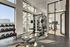 Modern gym with floor-to-ceiling windows, featuring state-of-the-art equipment including weights, squat rack, and exercise bikes, bathed in natural light.