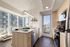 Modern apartment kitchen with sleek appliances, large windows offering stunning city views, and elegant light wood cabinetry.