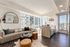 Modern apartment living room with stylish decor, featuring a cozy sofa, chic round coffee table, and sunlit kitchen area with skyline views.