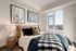 Bright and airy bedroom with chic decor, elegant framed art, and a stunning city view through a large window.