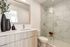 Bright and modern bathroom with elegant wood cabinetry, large mirror, and a stylish glass shower featuring marble tiles.