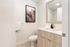Modern bathroom with sleek wood-finished vanity, large mirror, and elegant wall art, creating a serene and sophisticated atmosphere.