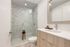 Elegant bathroom featuring a marble-tiled walk-in shower, sleek wooden vanity with modern fixtures, and ambient lighting.