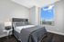 Elegant bedroom with modern decor, featuring a plush bed, sleek side table, and a large window showcasing breathtaking city views.