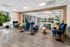 Elegant seating area in a modern apartment featuring plush blue chairs, stylish wooden tables, and vibrant green plants, complemented by large windows and sleek flooring.