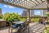 Charming outdoor patio with a pergola and string lights, surrounded by lush greenery and cityscape views, perfect for relaxing or entertaining.