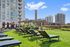 Elegant cityscape view from a modern apartment rooftop featuring stylish lounge chairs, vibrant greenery, and a picturesque pergola.