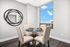 Chic dining area with modern circular mirror, elegant glass table, and upholstered chairs, offering stunning city views through large window.
