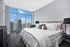 Luxurious bedroom with floor-to-ceiling windows offering stunning city skyline views, complemented by elegant decor and plush bedding.