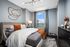 Elegant bedroom with modern decor, featuring a plush bed adorned with textured pillows and throws, a chic golden wall art, and a stunning city view through a large window.