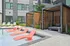 Luxurious apartment courtyard featuring a modern swimming pool with stylish red loungers, chic wooden cabanas, and lush greenery.