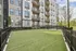 Modern apartment building with spacious balconies overlooking a pristine green lawn, enclosed by a stylish black fence.