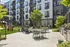 Modern apartment complex with inviting outdoor seating, lush greenery, and sleek barbecue area, perfect for social gatherings and relaxation.
