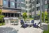Contemporary outdoor lounge area with modern seating, BBQ grills, and lush greenery against a stylish apartment backdrop.