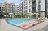 Modern apartment complex with stylish swimming pool surrounded by comfortable lounge chairs and vibrant greenery, perfect for relaxation.