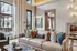 Modern apartment living room featuring a chic beige sofa with decorative pillows, stylish artwork, and expansive windows offering a glimpse of the outdoor patio.