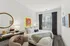 Chic bedroom with vibrant wall art, cozy bed, elegant workspace, and natural light filtering through large window blinds.