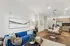 Modern open-concept living room with a vibrant blue sofa, stylish dining area, and sleek kitchen offering a warm and inviting atmosphere.