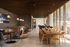 Elegant and contemporary lounge area with stylish leather seating, modern pendant lighting, and a long wooden communal table, offering panoramic city views through floor-to-ceiling windows.