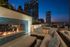 Luxurious rooftop lounge with cozy seating and a modern fireplace, overlooking a stunning city skyline at dusk.