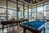 Luxurious entertainment room with pool table and shuffleboard, floor-to-ceiling windows showcasing stunning city views, and elegant outdoor seating.